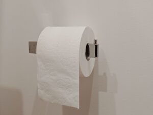 Moderne chromen wc rolhouder met een rol toiletpapier aan een witte wand.
