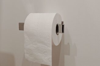 Moderne chromen wc rolhouder met een rol toiletpapier aan een witte wand.